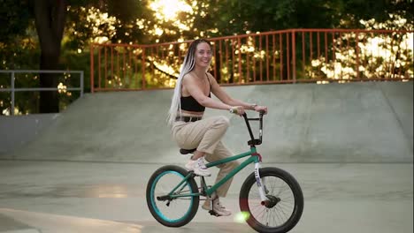 Encantadora-Joven-Montando-Bicicleta-BMX-Bajo-La-Luz-Del-Sol-En-El-Skatepark-Al-Aire-Libre.-Gente-Activa.-Chica-Guapa-Con-Rastas-Cabalgando-Libremente.