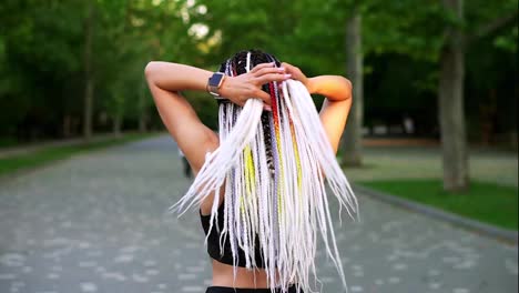 Black-and-white-dreadlocks-on-the-back-of-a-girl.-Rear-view-of-a-sporty-girl-knotting-hair-and-starting-to-run-in-the-green