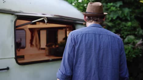 Man-in-a-hat-and-blue-shirt-came-to-the-window-in-trailer-truck,-house-on-wheels-and-sensually-kiss-his-wife-through-it.-Concept-of-vacation-or-life-in-a-van