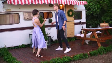 Stylish,-cheerful-couple-man-and-woman-smiling-while-dancing-together-near-house-on-wheels-outdoors.-Funky-dancing-in-front-the-trailer.-Retro-style-exterior.-Slow-motion