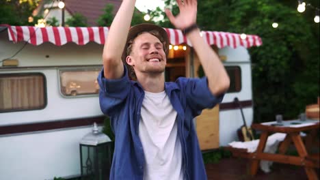 Happy-cheerful-man-in-casual-clothes-and-summer-hat-is-dancing-outdoors-in-front-the-trailer-truck.-Bearded-joyful-man-in-his-best-mood,-dancing-happily.-Slow-motion