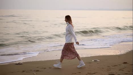 Girl-in-elegant-clothes-walks-along-the-seashore-view-from-the-side