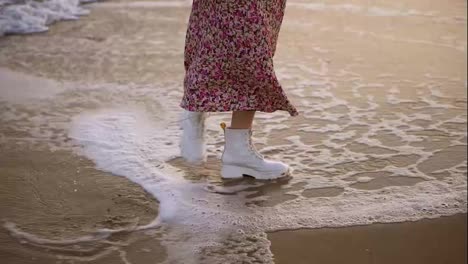 Girl-in-elegant-clothes-walks-along-the-seashore-stepping-on-foamy-waves