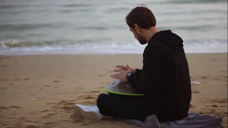 The-man-in-black-casual-playing-hang-sitting-on-the-beach-in-front-the-sea-alone-in-autumn