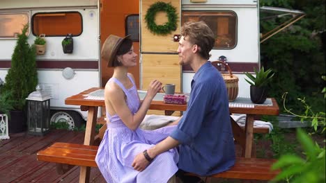 Portrait-of-cute-couple-man-and-woman-eating-raspberries-together-at-wooden-table-outdoors,-feeding-each-other,-kissing.-Happy-vacation-together-in-trailer