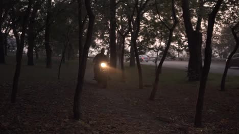 Big-guy-rides-a-motorcycle-cross-country-between-trees-or-forest-with-turned-on-headlight