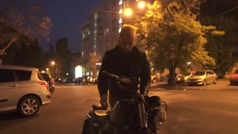 Handsome-rider-man-sitting-on-classic-style-motorbike,-turns-on-from-parking-place-at-night