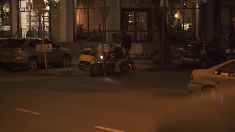 Attractive-rider-man-starting-from-parking-place-on-motorbike,-turns-on-and-riding-by-night-city-street