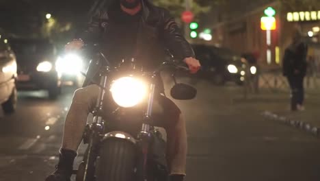 Front-view-of-a-bearded-motorcyclist-drives-a-bike-in-the-city-with-bright-headlight-at-night