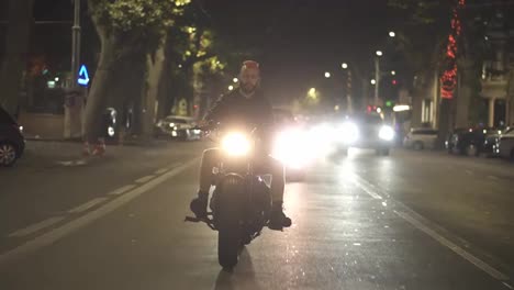 Front-view-of-a-brutal-motorcyclist-drives-a-bike-in-the-city-with-bright-headlight-at-night