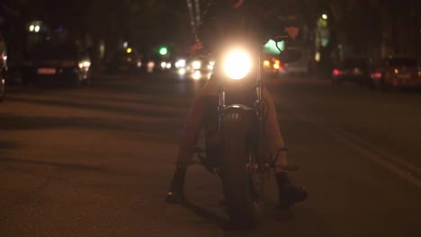 Bearded-rider-sitting-on-a-motocycle,-turning-higly-bright-the-headlight-standing-on-the-night-city-street
