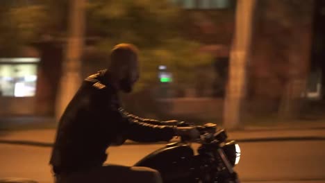 Side-view-of-a-brutal-man-riding-fast-his-motocycle-by-night-city-street