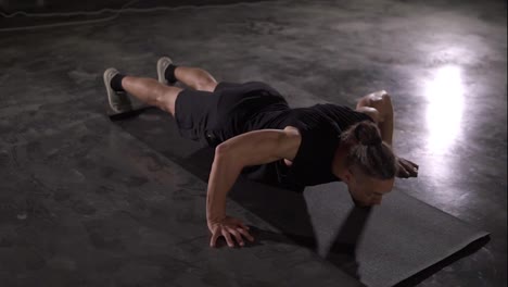 Caucasian-man-with-dreadlocks-in-black-sportswear-does-push-ups-in-empty-gym-or-studio.-Part-of-his-cross-fitness-workout-body-weight-training