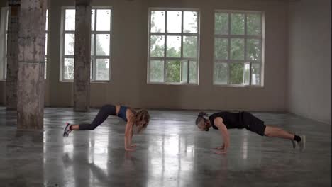 Man-and-woman-with-dreadlocks-in-fitness-studio-doing-exercises-together,-performing-push-ups-with-jumps-and-claps.-Loft-interior.-Side-view