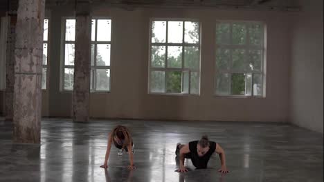 Man-and-woman-with-dreadlocks-in-fitness-studio-doing-exercises-together,-performing-push-ups-with-jumps-and-claps.-Loft-interior.-Front-view
