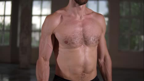 Shirtless-muscular-man-doing-workout-with-dumbbells-and-sweat-on-his-body.-Close-up-of-man's-torso-during-workout