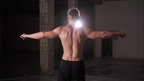 Starker-Bodybuilder-Posiert-Nach-Dem-Training-Mit-Scheinwerferlicht-Auf-Dem-Rücken-Und-Zeigt-Seinen-Körper-Und-Seine-Muskeln,-Die-Die-Hände-Ausbreiten