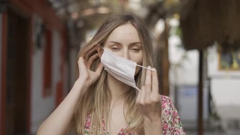 Blonde-woman-putting-on-medical-mask-for-coronavirus-protection-outdoors