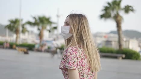 Beautiful-woman-in-dress-and-medical-mask-walking-alone-on-city-pier