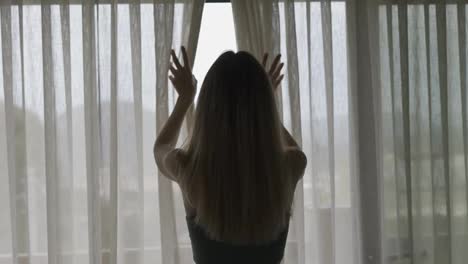 Rear-back-view-of-woman-opening-curtain-lace-standing-at-modern-hotel-looking-through-window