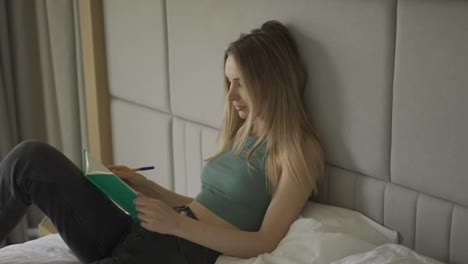Young-woman-is-sitting-on-bed-at-home-and-writing-in-diary