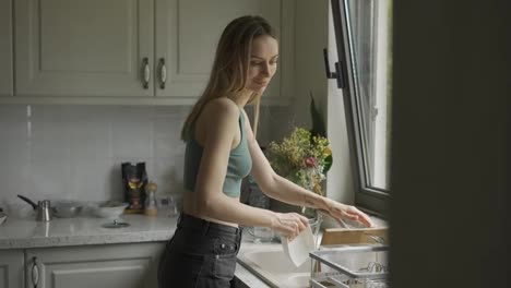 Woman-washing-dishes-under-running-water-in-sink-at-modern-kitchen