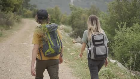 A-happy-couple-backpackers-walking-by-forest's-path,-rear-view