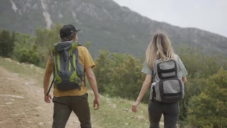 A-happy-couple-backpackers-hiking-by-hills,-exploring-new-places
