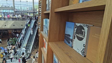 Focus-on-books-in-shelf-as-crowds-come-down-the-escalator