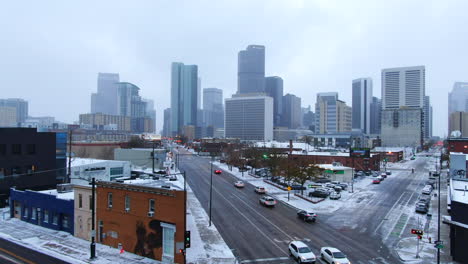 Aerial-cinematic-drone-downtown-Denver-Colorado-city-buildings-snowing-freezing-cold-winter-day-gray-bird-dramatic-city-landscape-car-traffic-passing-cross-intersection-upward-dolly-jib-movement