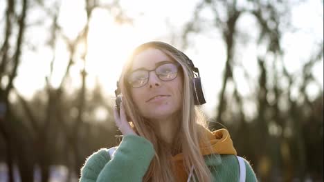 Portrait-of-a-woman-in-winter-park,-listening-to-music-on-the-phone-using-headphones,-smiling