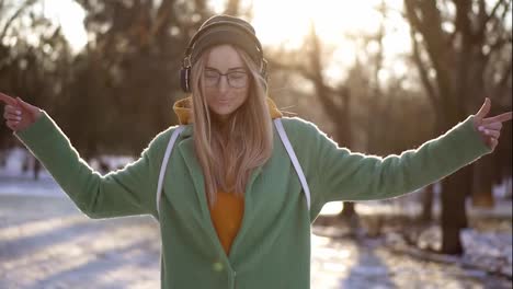 Beautiful-woman-walk-and-dance-in-winter-park,-listening-to-music-on-the-phone-using-headphones