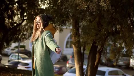 Blonde-woman-dance-in-winter-park,-listening-to-music-on-the-phone-using-headphones,-spinning-around