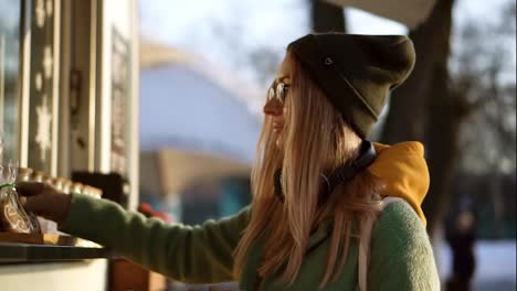 Woman-considers-gingerbread,-taking-a-hot-coffee-in-street-kiosk-on-winter-walk
