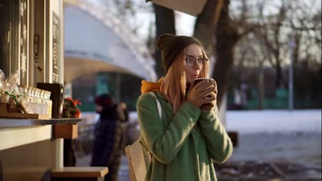 Cheerful-woman-drinking-a-hot-drink,-steam-from-hot-coffee-or-tea-in-the-city-park