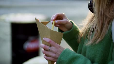 Woman-eating-french-fries-outdoors-on-winter-street-dip-in-ketchup