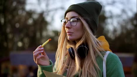 Blonde-girl-eating-french-fries-outdoors-on-winter-street-dip-in-ketchup