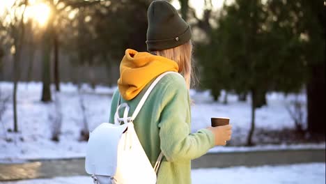 Woman-walking-with-hot-drink-by-winter-city-park,-enjoy-weather,-side-view