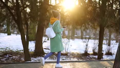 Woman-walking-with-hot-drink-by-winter-city-park-or-forest-in-slow-motion