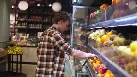 Man-selecting-fresh-fruits-in-grocery-store-produce-department-and-putting-it-in-plastic-bag.-Young-guy-is-choosing-oranges-in-supermarket-and-putting-them-into-shop-basket.-Side-view