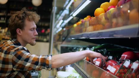 A-caucasian-man-in-plaid-shirt-shopping-for-fruits-and-vegetables-in-produce-department-of-a-grocery-store-supermarket.-Choosing-perfect-fresh-tomatoes-from-the-lower-shelf.-Side-view