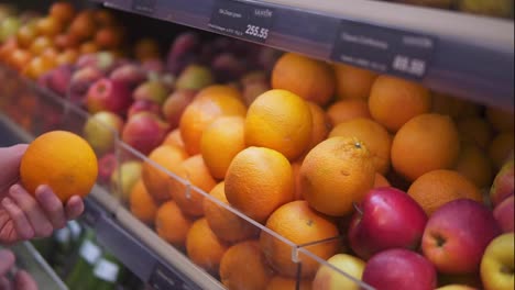 Man's-hand-selecting-fresh-fruits-in-grocery-store-produce-department-from-shelf.-Young-guy-is-choosing-oranges-in-supermarket.-Side-view.-Close-up