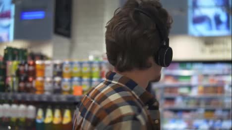 Im-Supermarkt:-Kaukasischer-Mann-Mit-Kopfhörern-Geht-Durch-Die-Warenabteilung-Des-Ladens-Und-Stöbert.-Folgende-Rückansicht