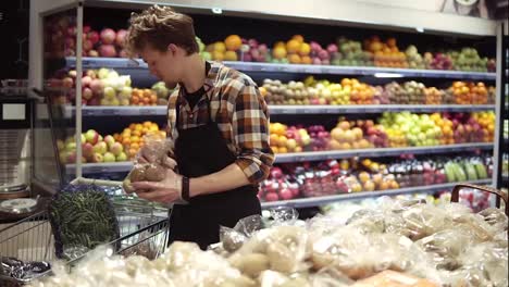 Busy-caucasian-young-worker-arranging-vegetables-on-shelves-at-grocery-shop.-Guy-in-apron-filling-up-storage-rack-with-healthy-organic-potatos-in-supermarket