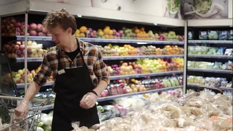 Busy-caucasian-young-worker-arranging-vegetables-on-shelves-at-grocery-shop.-Guy-in-apron-filling-up-storage-rack-with-healthy-organic-potatos-in-supermarket.-Slow-motion