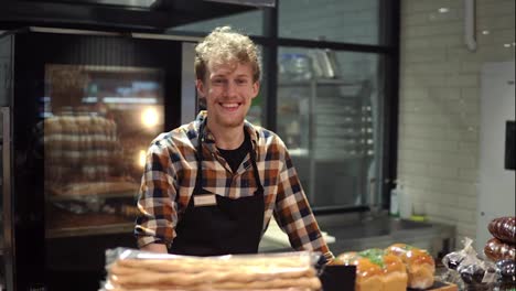 Portrait-of-the-handsome-man-baker-in-plaid-shirt-and-apron-smiling-to-the-camera-and-posing-in-the-bakery-shop.-Close-up.-Indoor