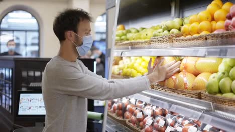Man-in-mask-takes-a-fresh-citrus-from-the-food-shelf.-Shopper-choosing-pummelo-at-grocery-store