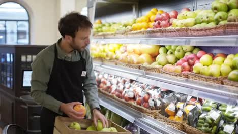 Ein-Vielbeschäftigter-Verkäufer-Stellt-Obst-In-Die-Regale-Der-Gemüseabteilung-Im-Supermarkt,-Der-Bärtige-Mann-Trägt-Eine-Schürze