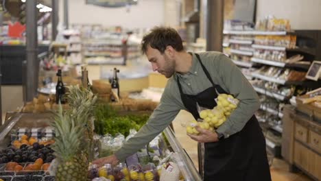 Grocery-store-worker-caucasian-bearded-guy-arranging-packed-potato-in-apron-at-modern-organic-supermarket-grocery-store