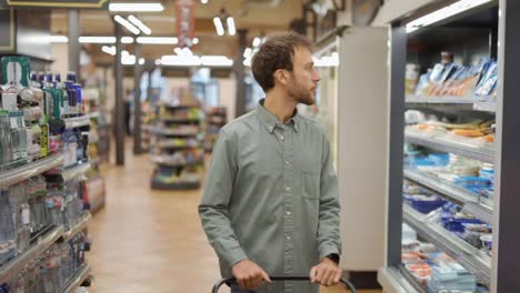 Happy-man-in-shirt-walking-with-a-cart-through-the-supermarket-choosing-groceries